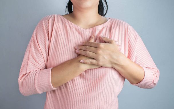 Aziatische jonge vrouw die lijdt aan pijn op de borst veroorzaakt door hart-en vaatziekten. - Foto, afbeelding
