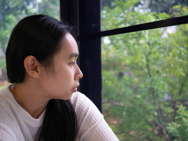 Portrait of Asian young sad woman looking through a window in a rainy day at home. - Photo, Image