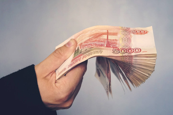 Mavi arka planda genç bir iş adamının elinde çok para var. 5.000 ruble değerinde bir yığın Rus rublesi. Başarılı iş adamı - Fotoğraf, Görsel