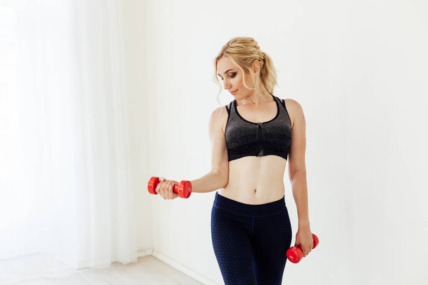 Beautiful blonde woman sports with fitness dumbbells in the hall - Photo, Image