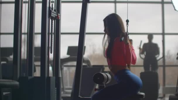 A lány megrázza a hátát edzés közben. Képzés egy szobában nagy ablakok a háttérben egy nő használ egy ellipszoid és egy futópad - Felvétel, videó