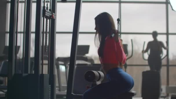 Vrouw schudt haar rug bij een training in de sportschool. Training in een ruimte met grote ramen op de achtergrond een vrouw gebruikt een ellipsoïde en een loopband - Video