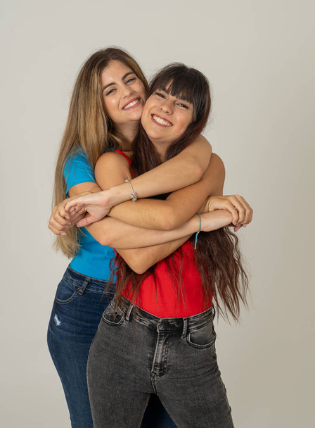 Two stylish girl friends having fun laughing, hugging and kissing. Blonde and brunette young women models enjoying time together and posing against neutral background. Friendship, love and care. - Foto, Imagen