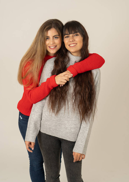 Two stylish girl friends having fun laughing, hugging and kissing. Blonde and brunette young women models enjoying time together and posing against neutral background. Friendship, love and care. - Foto, imagen