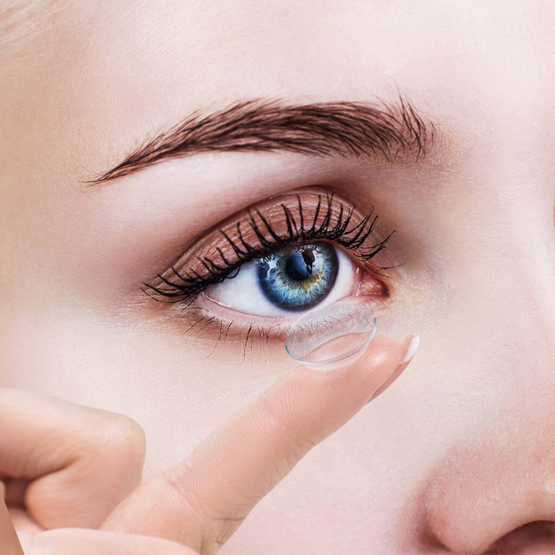 Contact lens on index finger near blue female eye. - Foto, immagini