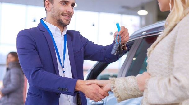 Car salesman sells a car to happy customer in car dealership and hands over the keys. - Foto, imagen