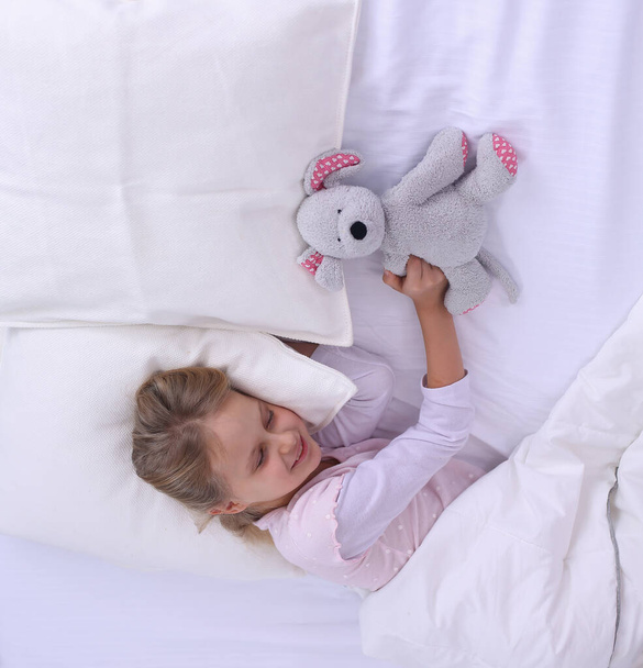Kleines Mädchen schläft im Bett mit einem Spielzeug-Teddybär. - Foto, Bild