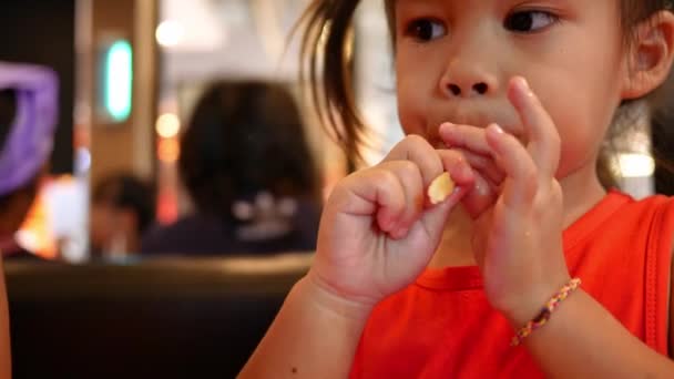 Klein Aziatisch meisje met haar zus die gefrituurde kip en frietjes eet in restaurant. Gezondheidszorg en voedselconcept. - Video