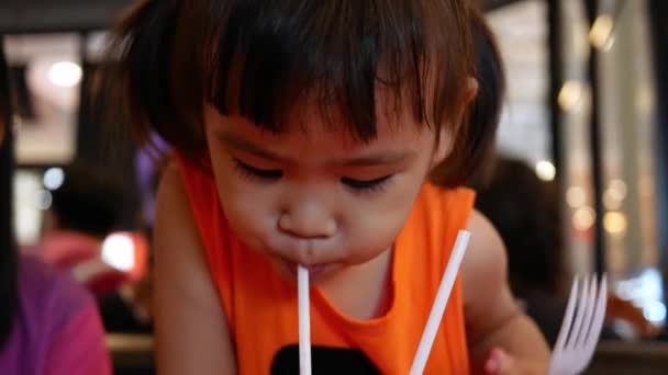 Little Asian child girl with her sister sipping her drink together while sitting wait food in restaurant. Selective focus. - Footage, Video