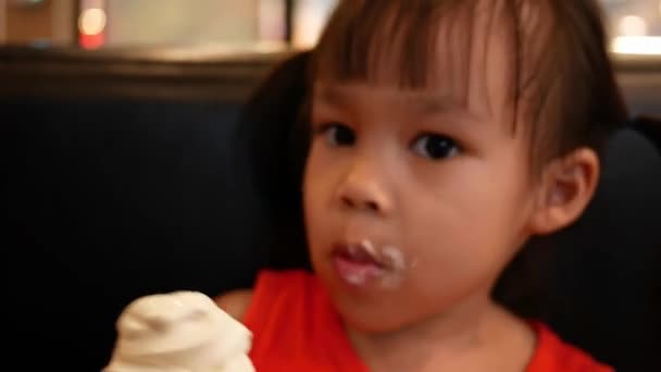Очаровательная маленькая азиатская девочка держит и ест мороженое с конусом в ресторане
. - Кадры, видео