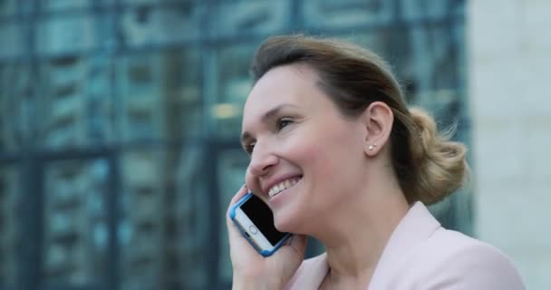 Closeup face of an adult woman talking by mobile phone.  Smiling caucasian woman calling by  cell phone, outdoors. Happy lady  with mobile phone.  Real time. 4k.  - Imágenes, Vídeo