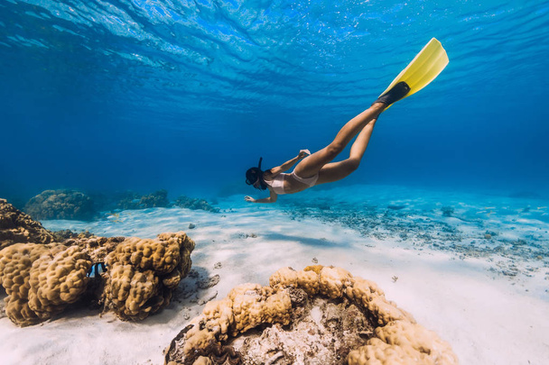 Kadın serbest dalgıç sarı yüzgeçleriyle kumlu denizde süzülüyor. - Fotoğraf, Görsel