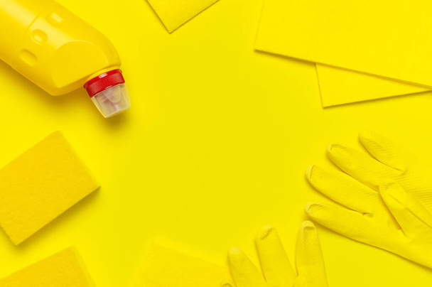 House cleaning concept. Household chemicals, disinfectant, bleach, antibacterial gel, yellow rubber gloves, sponge, rags on yellow background. Flat lay top view copy space. Cleaning accessories - Photo, Image