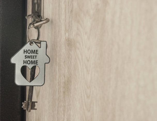 huissleutel op een huis vormige Zilveren sleutelhanger in het slot van een deur - Foto, afbeelding