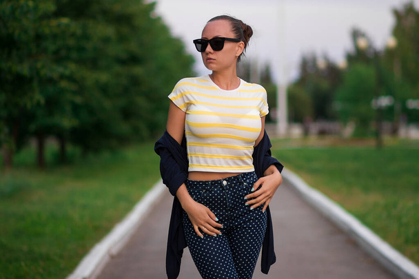 Magabiztos, napszemüveges fiatal nő a sétányon a parkban - Fotó, kép