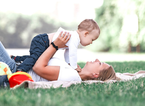 mom and her little son play together, lying on the lawn . - Foto, afbeelding