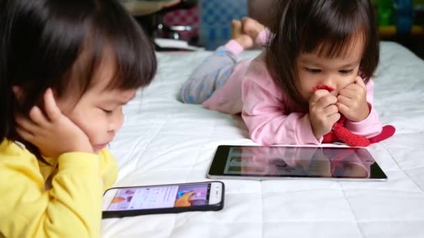 Asijská holčička se dívá na smartphone na posteli. Kluk závislý na mobilních telefonech. - Záběry, video