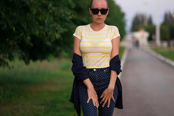 Park yolunda güneş gözlüklü, kendine güvenen genç bir kadın. - Fotoğraf, Görsel