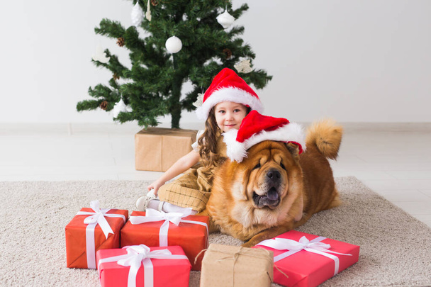 Kinder-und Haustier-Konzept - niedliches Mädchen mit Chow-Hund sitzt neben dem Weihnachtsbaum. Frohe Weihnachten und frohe Feiertage. - Foto, Bild