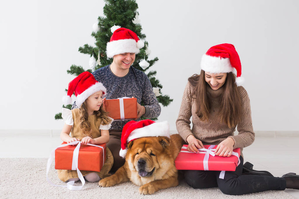 Pet, holidays and festive concept - Family with dog are sitting on floor near christmas tree. - Photo, Image