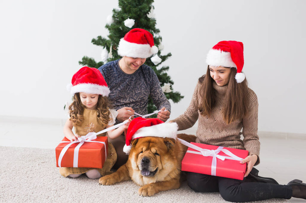 ペット、休日、お祝いのコンセプト-犬と家族はクリスマスツリーの近くの床に座っています. - 写真・画像