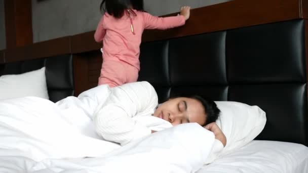 Cute Asian little girl wakes her mother up while lying on the bed at home in the morning. - Materiał filmowy, wideo