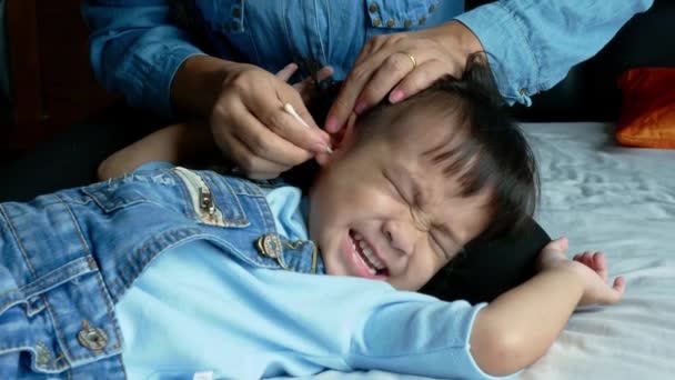 Asiatico madre utilizzando un batuffolo di cotone per pulire le orecchie bambina sul letto. Concetto sanitario
. - Filmati, video