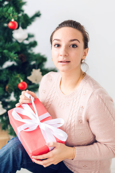 christmas, x-mas, winter, happiness concept - girl opens a gift against the background of the Christmas tree. Happy young woman celebrating Christmas - Photo, image