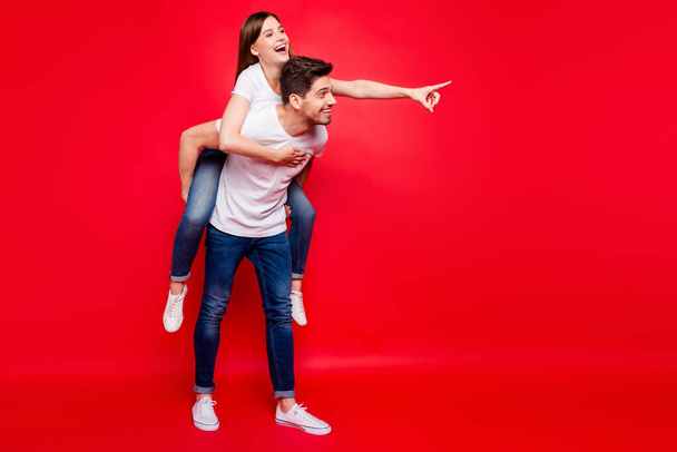 Full length body size photo of cheerful nice couple of boyfriend girlfriend pointing showing way in jeans denim white t-shirt footwear boyfriend carrying funky toothy isolated vivid color background - Fotografie, Obrázek