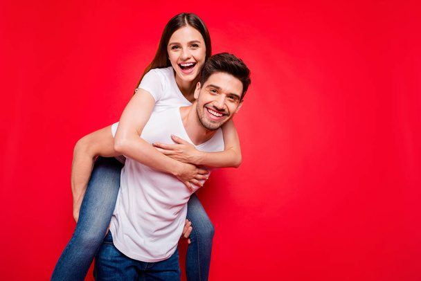 Photo of cheerful positive pretty couple of two people piggyback girl hugging riding guy in jeans denim white t-shirt carrying near empty space isolated vivid color background - Valokuva, kuva