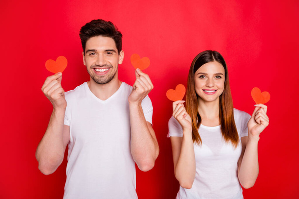 Photo of cheerful positive pretty nice charming couple of two people spouses demonstrating two postcards heart shape smiling toothily in white t-shirt isolated vivid color background - Foto, Imagem