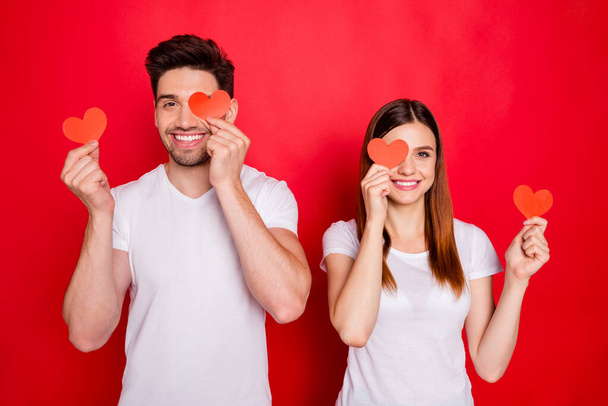 Photo of cheerful positive nice pretty couple of boyfriend girlfriend smiling toothily covering their eye showing their love with red heart white t-shirt postcards isolated vivid color background - Fotografie, Obrázek