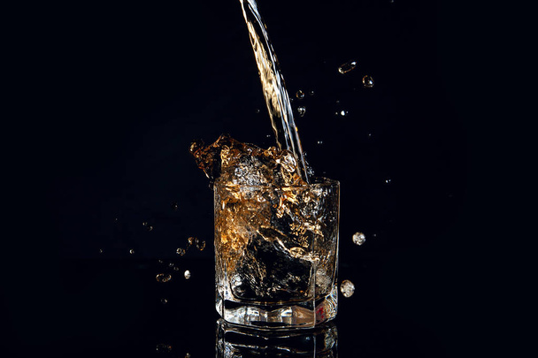 Whisky nalil do sklenice s ledem, samostatný na černém pozadí - Fotografie, Obrázek