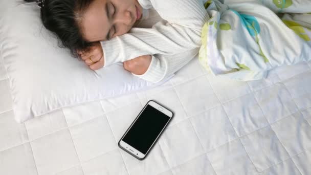 Asian young woman is sleepy while alarm clock and pressing snooze alarm on mobile phone in the morning. - Filmati, video