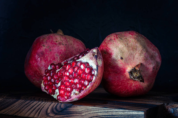 Chutné a zralé granátové jablko na černém pozadí, na řezací desce, rustikální styl - Fotografie, Obrázek