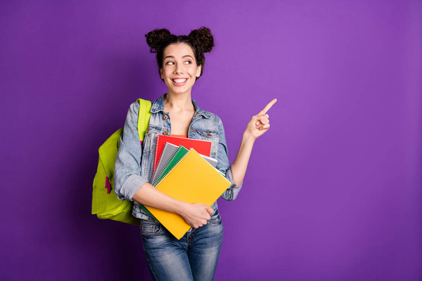 Portrait of positive cheerful high school girl point index finger hold notebooks present academic courses information wear stylish trendy outfit green bag isolated over violet color background - Photo, image