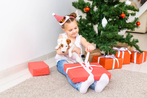 Christmas, pets and holidays concept - Child in santa hat with a jack russell terrier puppy - Photo, Image