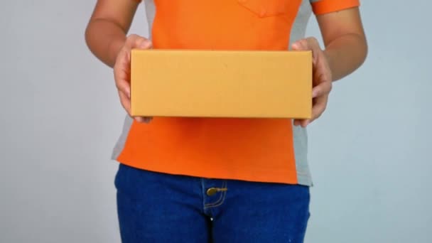 De cerca la mano de una joven mujer sosteniendo una caja de paquetes y presentándote, aislada sobre un fondo gris
. - Metraje, vídeo
