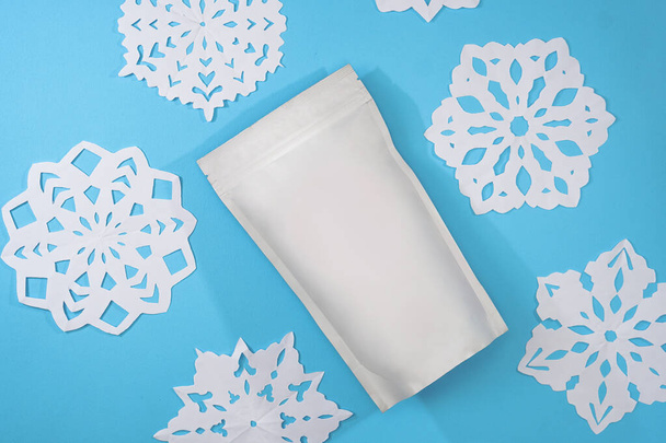 Vorlage für Papier ökologische Tasche zur Lagerung von Kaffee, Tee auf einem isolierten blauen Hintergrund mit handgemachten Schneeflocken. Vakuumverpackungen für Weihnachten und Neujahr - Foto, Bild