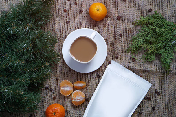Πρότυπο του χαρτιού οικολογική τσάντα για την αποθήκευση καφέ, τσάι σε φόντο υφής και ένα φλιτζάνι καπουτσίνο με μανταρίνια. Κενή συσκευασία για δώρο Χριστουγέννων και Πρωτοχρονιάς - Φωτογραφία, εικόνα