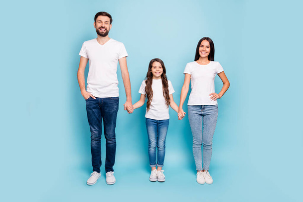 Full body photo of cheerful content big three people with brunette hair hold hand enjoy family day holidays wear white t-shirt denim jeans sneakers isolated over pastel blue color background - Zdjęcie, obraz