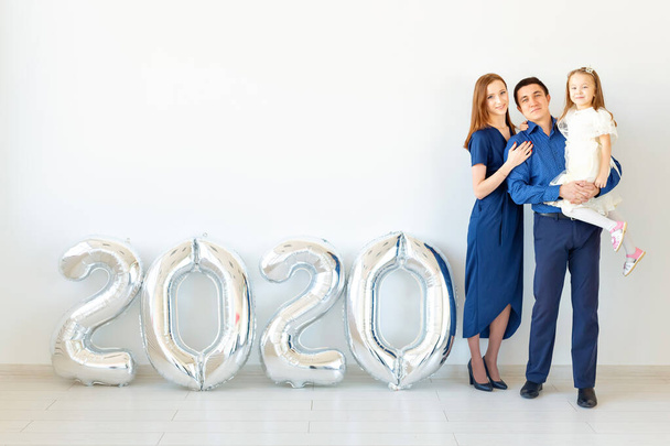 Giovane famiglia felice madre e padre e figlia in piedi vicino palloncini a forma di numeri 2020 su sfondo bianco. Anno nuovo, Natale, vacanza
 - Foto, immagini