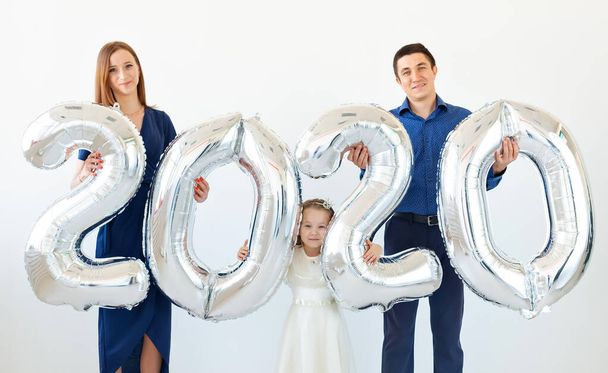 junge glückliche Familienmutter und Vater und Tochter mit Luftballons in Form von Ziffern 2020 auf weißem Hintergrund. Neues Jahr, Weihnachten, Feiertag - Foto, Bild