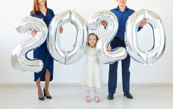 Jeune famille heureuse mère et père et fille tenant des ballons en forme de nombres 2020 sur fond blanc. Nouvel an, Noël, vacances
 - Photo, image