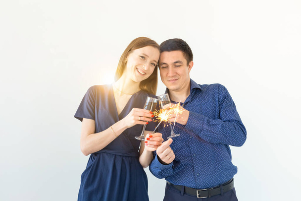 Homem e mulher comemorando a festa de Natal ou Ano Novo com luzes de Bengala e copos de champanhe no fundo branco
. - Foto, Imagem
