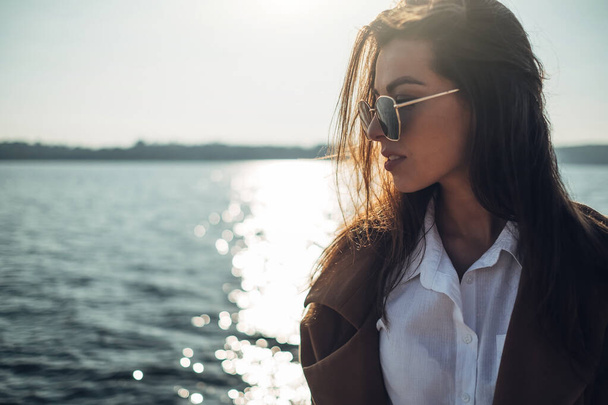 Piękna młoda stylowa dziewczyna w płaszcz Chodzenie w Spring Beach o zachodzie słońca - Zdjęcie, obraz