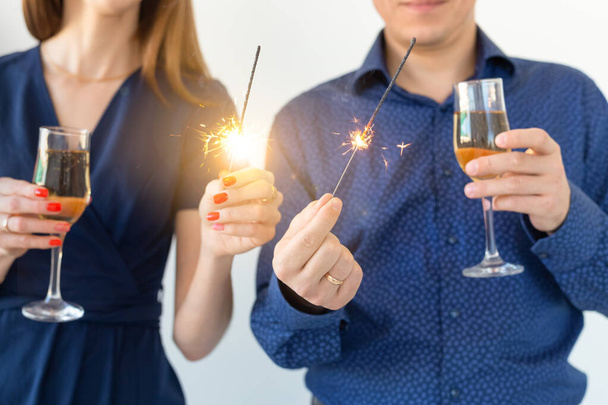 Close-up of man and woman celebrating Christmas or New Year eve party with Bengal lights and glasses of champagne. - Фото, изображение