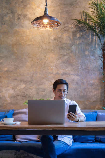 Férfi nézi a mobiltelefon, miközben dolgozik laptop kávézóban. - Fotó, kép