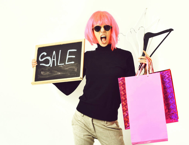 девушка в парике холдинг пакет, вешалки, доска с надписью продажи - Фото, изображение