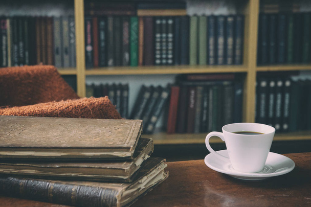 A pihenés édes pillanatai könyvekkel és egy csésze kávéval. Egy férfi egy karosszékben egy macskával. Vintage könyvek, poharak, könyvtár. - Fotó, kép